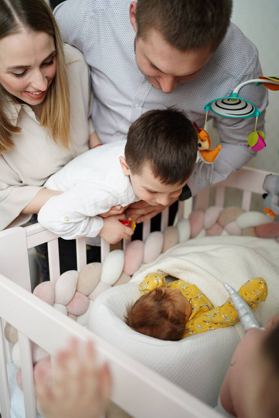 mom, dad and son are standing at the crib with a newborn baby. - Foto, imagen