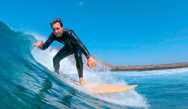Κοντινό πλάνο: Happy αρσενικό surfer ιππασία ένα κύμα και δίνοντας την κάμερα την πινακίδα Shaka. - Φωτογραφία, εικόνα