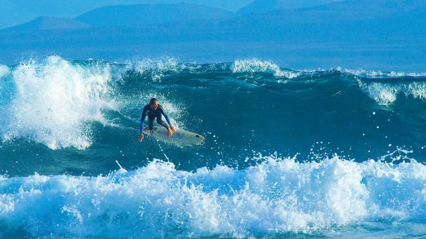 Nagy hordóhullám taszítja a fiatal szörföst a Kanári-szigetek partvonala felé.. - Fotó, kép