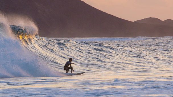 Athletic surfer dude carving large breaking wave at colorful summer sunset. - 写真・画像