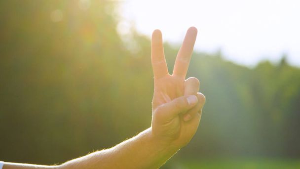LENS FLARE, DOF: Bright sunbeams shine on male hand and showing the peace sign. - Φωτογραφία, εικόνα