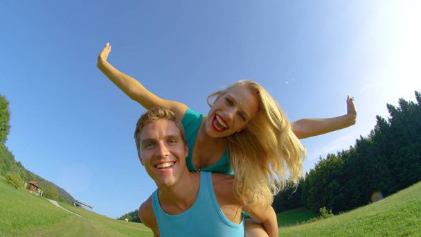 SUN FLARE: Girl outstretches arms while getting a piggyback ride from boyfriend. - Foto, imagen
