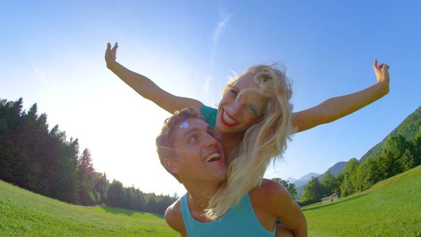 LENS FLARE: Happy man looks into the camera while giving girl a piggyback ride. - Photo, Image