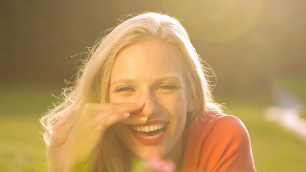 LENS FLARE: Beautiful young woman lying in a meadow and laughing to a joke. - Foto, imagen