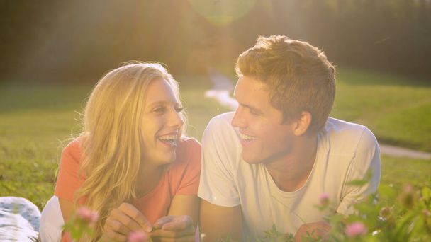 LENS FLARE: Couple lying in the grassfield laughs while filming a video blog. - Foto, Imagen