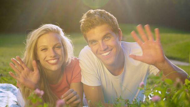 PORTRAIT: Glückliches Paar winkt nach Dreharbeiten auf der sonnigen Wiese in die Kamera. - Foto, Bild