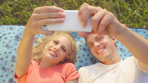CLOSE UP: Cheerful couple laughing and taking selfies while lying on a blanket. - Foto, Imagem