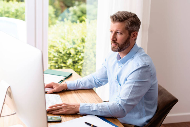 Businessman sitting at desk behind his computer while working from home.  - Photo, image