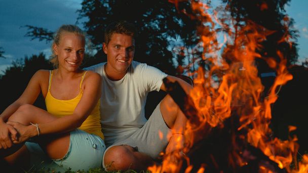 CLOSE UP: Glückliches Paar sitzt während einer Zeltreise am knisternden Feuer. - Foto, Bild