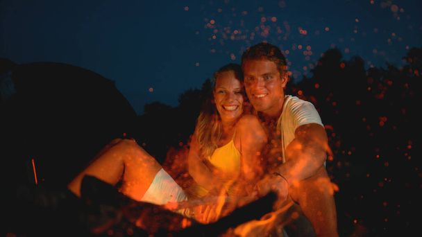Uzavřeno: Šťastný pár sedící u táboráku v romantickém letním večeru. - Fotografie, Obrázek