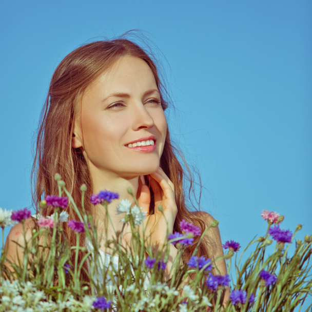 Beautiful young woman among flowers and blue sky - Фото, зображення