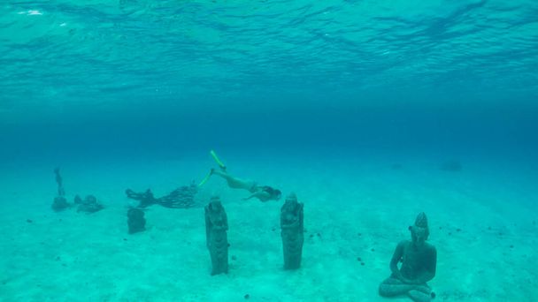 UNDERWATER: Curious female traveler diving around the ancient Buddha statues. - Фото, изображение