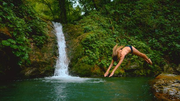 Unrecognizable energetic woman dives head first into refreshing emerald water. - Photo, Image