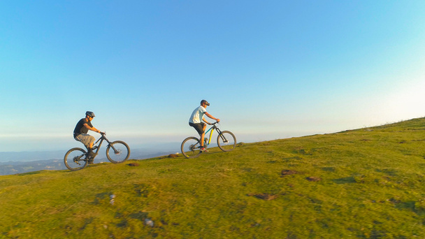 Два горных велосипедиста едут на электрических велосипедах по крутому травянистому холму
. - Фото, изображение