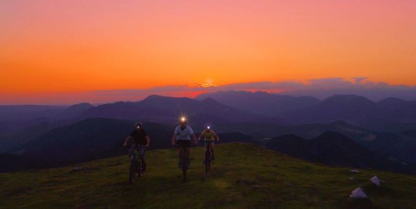 AERIAL: Volando frente a los ciclistas de montaña pedaleando sus bicicletas cuesta arriba por la noche
 - Foto, imagen