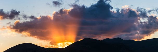 Погляд сонця на силует скелястих гір. Campo Imperatore, Gran Sasso, Apennines, Італія. Сонячні промені і барвисті хмари на драматичному гірському хребті.. - Фото, зображення