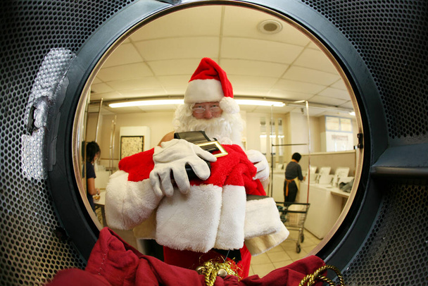 Άγιε Βασίλη. Χριστούγεννα. Ο Άγιος Βασίλης πλένει τα ρούχα του στα πλυντήρια πριν τα Χριστούγεννα. Συγκεντρώσου στα ρούχα του Άη Βασίλη. Ο Άγιος Βασίλης πλένει τα ρούχα του σε ένα χαλάκι πλυντηρίου πριν τα Χριστούγεννα. Ο Άγιος Βασίλης χρειάζεται καθαρά ρούχα. Καλά Χριστούγεννα. Καλές γιορτές..  - Φωτογραφία, εικόνα