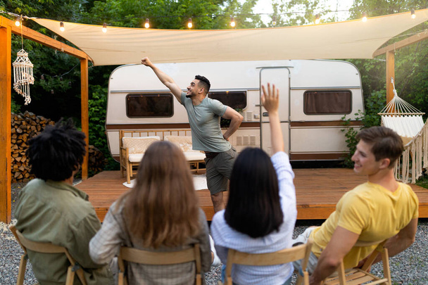 Diverse jonge vrienden spelen poppenkast in de buurt van camper, proberen te raden woord tijdens outdoor party - Foto, afbeelding