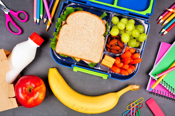 Healthy school lunch box with school supplies. Top down view over a chalkboard background. - 写真・画像