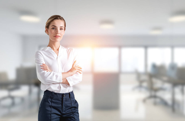 Confident attractive business woman in crossed arm pose is pondering how to optimize business process. Panoramic international consulting office on background. - Zdjęcie, obraz