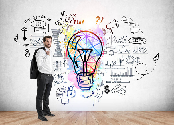 Handsome businessman in white shirt holding his jacket, concrete wall with colorful light bulb sketch. Launch a new business start up idea - Фото, зображення