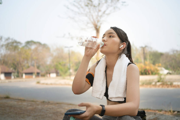 Nuori nainen lenkkeilijä juo makeaa vettä muovipullosta juoksemisen jälkeen puistossa. - Valokuva, kuva