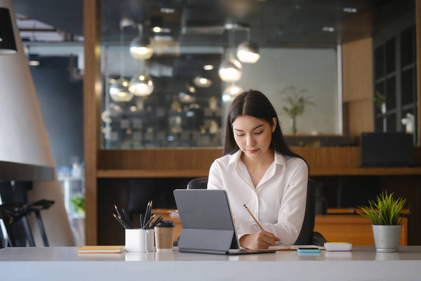 Молодая предпринимательница, сидящая на современном рабочем месте и работающая с планшетом. - Фото, изображение