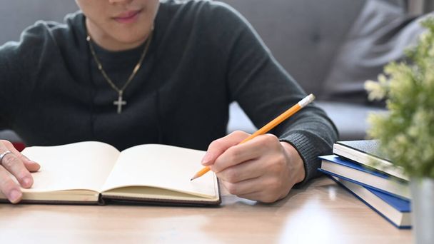 Közelkép a fiatal diák férfi írás notebook, miközben ül a nappaliban. - Fotó, kép