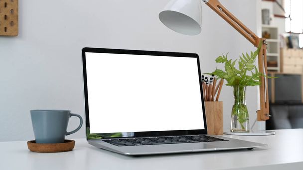 Нарисуйте ноутбук с чистым экраном, кофейной чашкой и держателем карандашей на белом столе в домашнем офисе. - Фото, изображение