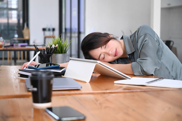Κουρασμένη νεαρή υπάλληλος γραφείου που κοιμάται στο γραφείο της. - Φωτογραφία, εικόνα