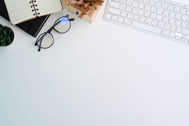 Bovenaanzicht van witte bureau met toetsenbord, bril en notebook. Kopieer ruimte voor reclame tekst. - Foto, afbeelding