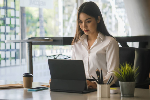 Atractiva trabajadora de oficina concentrada trabajando en tableta de computadora en moden office. - Foto, imagen