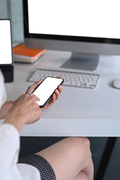 Gehakt schot van zakenvrouw werken met meerdere apparaten en het houden van smartphone tijdens het zitten op kantoor. - Foto, afbeelding