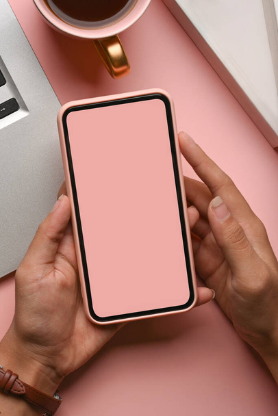 Vista de cerca de las manos femeninas que sostienen el teléfono móvil de la maqueta sobre fondo rosa pastel. - Foto, imagen