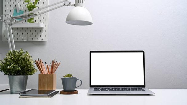 домашній офісний стіл з комп'ютерним ноутбуком, чашкою кави, цифровим планшетом, домашнім заводом та тримачем олівців на білому столі
. - Фото, зображення