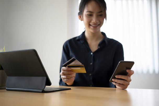 スマートフォンを使用して幸せな若いアジアの女性とオンライン銀行やオンラインショッピングのためのクレジットカードを保持. - 写真・画像