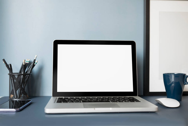 Laptop-Attrappe mit weißem Bildschirm, Handy, Kaffee und Schreibwaren auf dunkelblauem Tisch. - Foto, Bild