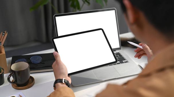 Tylny widok biznesmena pracujących online z domu z laptopem komputerowym i tabletem cyfrowym. - Zdjęcie, obraz