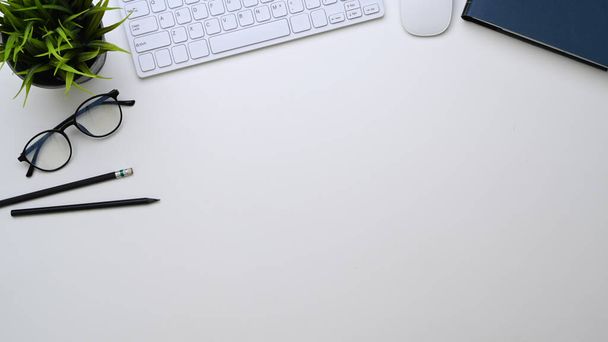Vue du dessus du bureau avec lunettes, clavier, crayons, plante et espace de copie sur fond blanc.  - Photo, image