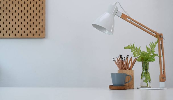 Egyszerű munkahely lámpával, ceruzatartóval, kávéscsészével és növényekkel az irodai asztalon. - Fotó, kép