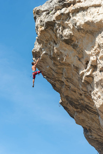 Rock climber hanging on his hands at top of peak - Photo, Image