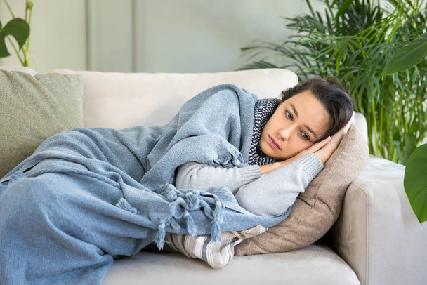 Больная женщина лежит дома на диване под одеялом - Фото, изображение