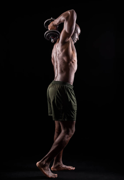 Вид сзади на мускулистого человека, стоящего, делая упражнения на трицепсы  - Фото, изображение