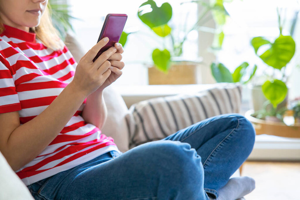 Young woman using mobile phone while sitting a sofa at home  - 写真・画像