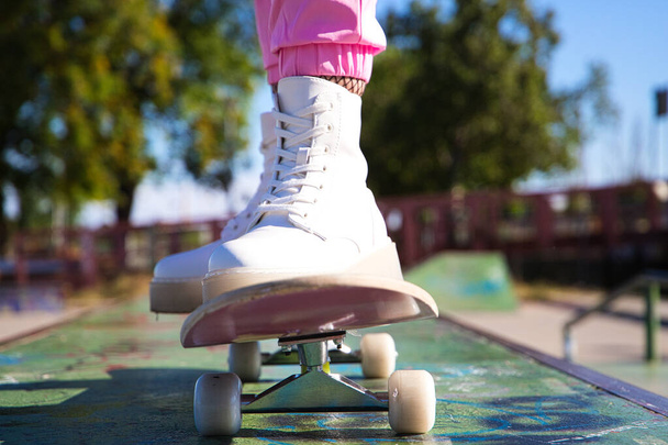 detaily dívčích nohou na skateboardu. Ta holka má na sobě růžové kalhoty a bílé boty. Je slunečný den. - Fotografie, Obrázek
