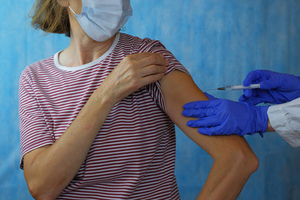 Impfung des Patienten. Ein Arzt gibt einer älteren Frau zu Hause eine Spritze. Eine Krankenschwester hält eine Spritze, um einen Impfstoff gegen Covid-19 oder Coronavirus herzustellen. - Foto, Bild
