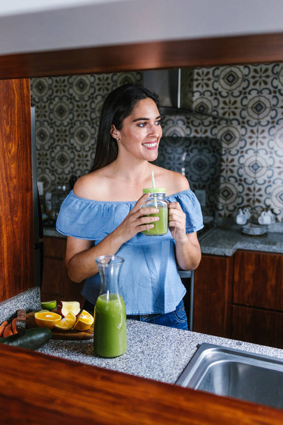 Mujer Latina haciendo batido verde o jugo de desintoxicación en la cocina en el hogar en concepto de alimentación saludable en México - Foto, imagen