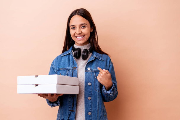 Joven mujer de raza mixta sosteniendo una pizza aislada persona señalando a mano a un espacio de copia de la camisa, orgulloso y seguro - Foto, imagen