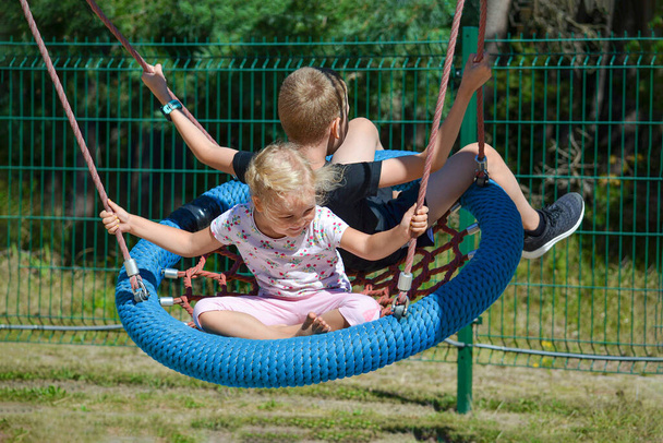 Παιδιά σε μια κούνια. Αγόρι και κορίτσι κάνουν κούνια στο πάρκο μια καλοκαιρινή μέρα. Πήγαινε στο πάρκο διασκέδασης των παιδιών. banner με θέση για κείμενο - Φωτογραφία, εικόνα