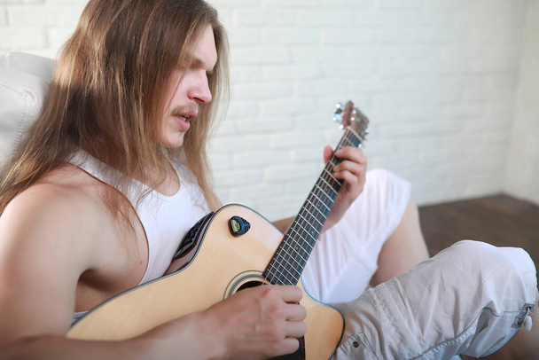 Молодой человек с длинными волосами и акустической гитой - Фото, изображение